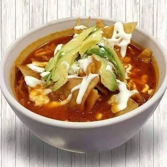 A bowl of Mexican soup topped with avocado and crema